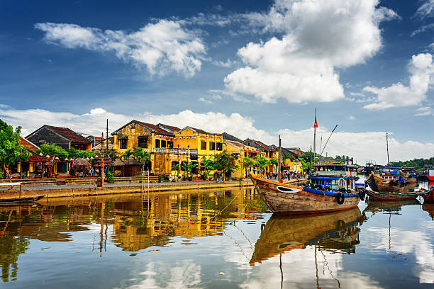 Wooden boats on the Thu Bon River, Hoi An, Vietnam Wooden boats on the Thu Bon River in Hoi An Ancient Town (Hoian), Vietnam. Yellow old houses on waterfront reflected in river. Hoi An is a popular tourist destination of Asia. hoi an stock pictures, royalty-free photos & images