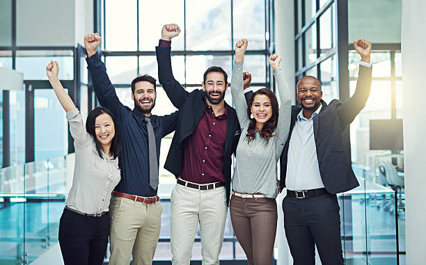 Positive teams produce positive outcomes Portrait of a diverse team of colleagues cheering at work cheering group of people success looking at camera stock pictures, royalty-free photos & images