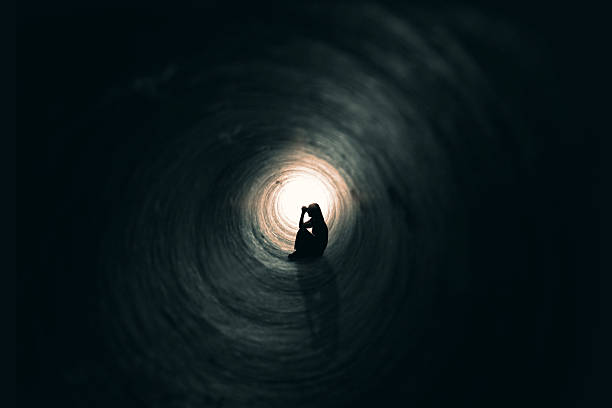 donna pregare in un luogo scuro - luce alla fine del tunnel foto e immagini stock