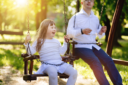 Happy child with down syndrome enjoying swing on playground
