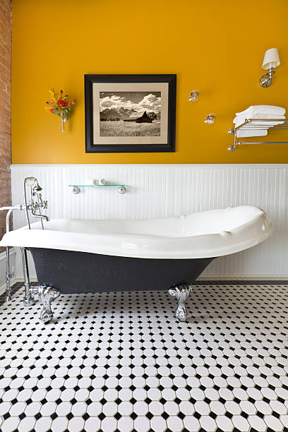 Contemporary Classic Bathroom Design with Claw Foot Tub A modern contemporary classic bathroom design, furnished with a classic painted cabinet, sepia toned picture on the wall, exposed brick wall and a window, a claw foot bath tub and black and white tile pattern on the floor. Photographed in vertical format. free standing bath stock pictures, royalty-free photos & images