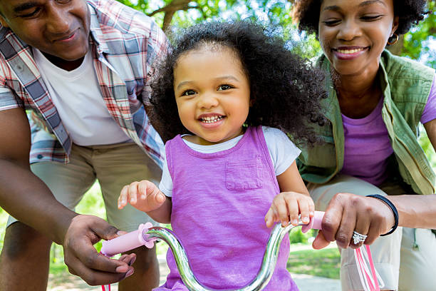 afro-américaine des parents apprend à sa fille à faire du vélo - family cheerful family with one child texas photos et images de collection