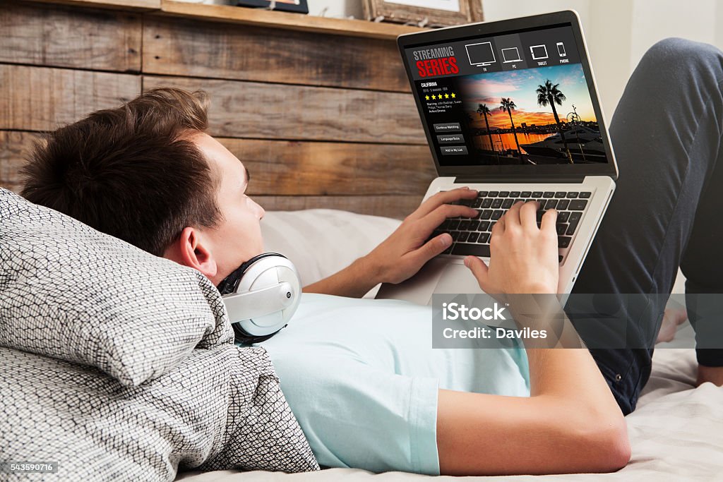 Watching tv series at home. Man watching streaming series in a laptop computer, lying in the bed. Downloading Stock Photo