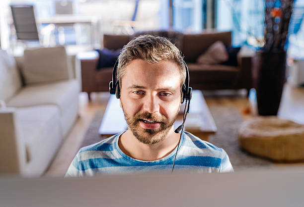 mann, arbeit von zu hause am computer tragen headset - working at home headset telecommuting computer stock-fotos und bilder