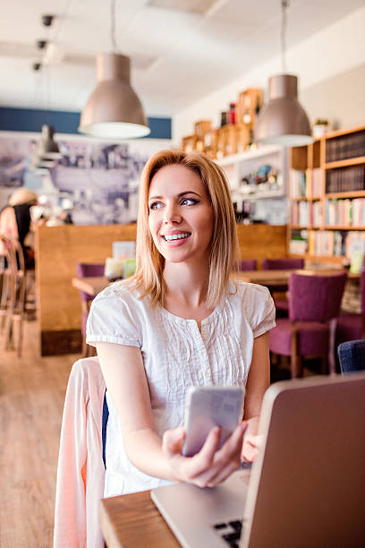 istock Blond woman with smartphone in cafe working on notebook 543597700