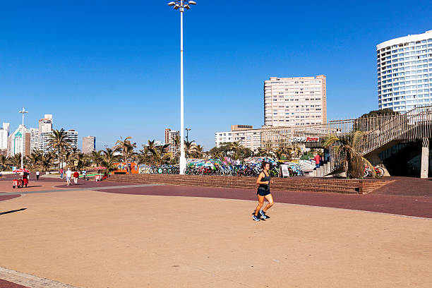 uma mulher correndo em um calçadão de frente para a praia - africa african descent south bicycle - fotografias e filmes do acervo