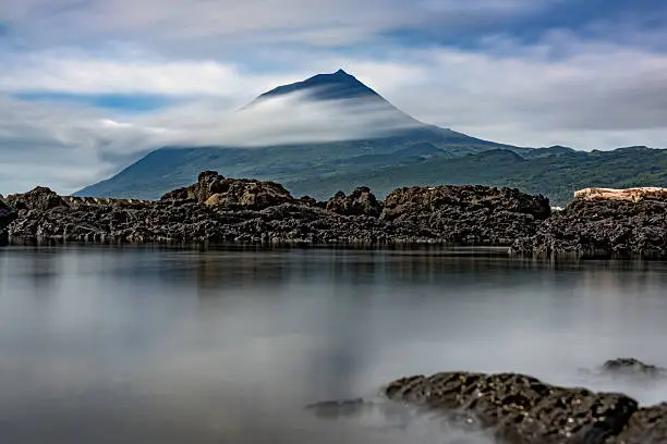 Long exposure landscape view of Pico volcano, surrounded by clouds washing in from the Atlantic ocean