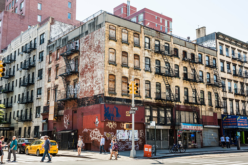 New York, USA - June 18, 2016: People walk next to old, rusty building with graffiti in Chinatown in New York City 