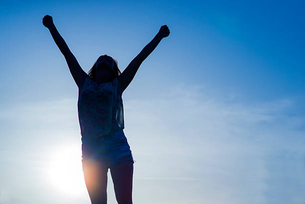 istock silhouette woman arms raised into sunset sky 543662422