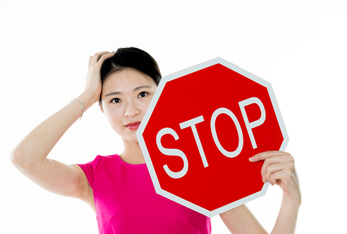 Young woman holding STOP sign against white background.