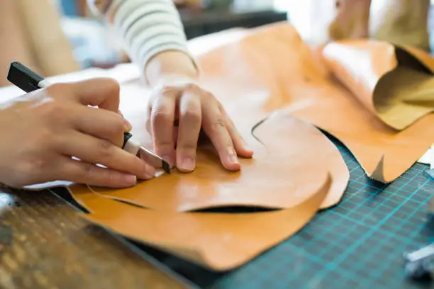 Close up view of a shoe maker as she cuts a pattern out of leather. Kyoto, Japan. May 2016