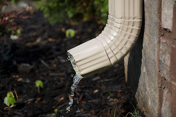 Gutter Downspout with water - side view A rain gutter downspout with water coming out from the side, with a flower bed in the background. Shallow Depth of Field. downspout stock pictures, royalty-free photos & images