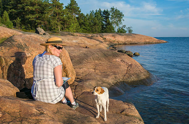 Side view of woman holding little dog around mountain lake, she looking forward and cute dog looking at camera.