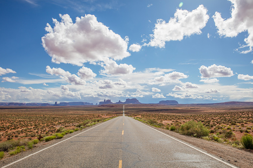 Endless highway wide angle view under beautiful cloudy summer sky to famous Monument Valley Buttes in Utah. Looking south on U.S. Route - Highway 163 from north of the Arizona–Utah border. Arizona - Utah, USA.