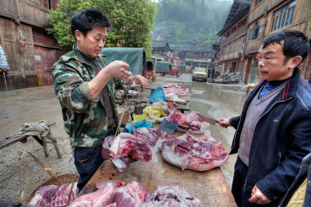 Asian butcher weighing pork for a buyer using Chinese scales. Zhaoxing Dong Village, Guizhou Province, China - April 8, 2010: A street vendor weighs pork on Chinese scales. pig farmer china stock pictures, royalty-free photos & images