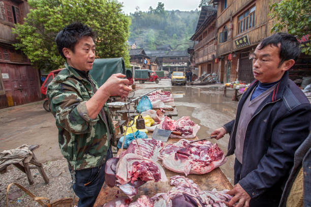 Street vendor weighs pork on Chinese scales. Zhaoxing Dong Village, Guizhou Province, China - April 8, 2010: Asian butcher weighing pork for a buyer using Chinese scales. pig farmer china stock pictures, royalty-free photos & images