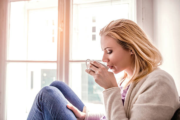 istock Woman on window sill holding a tea cup, drinking 543687538