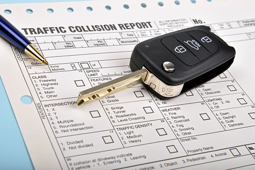 black car key with a traffic collision report and blue pen 