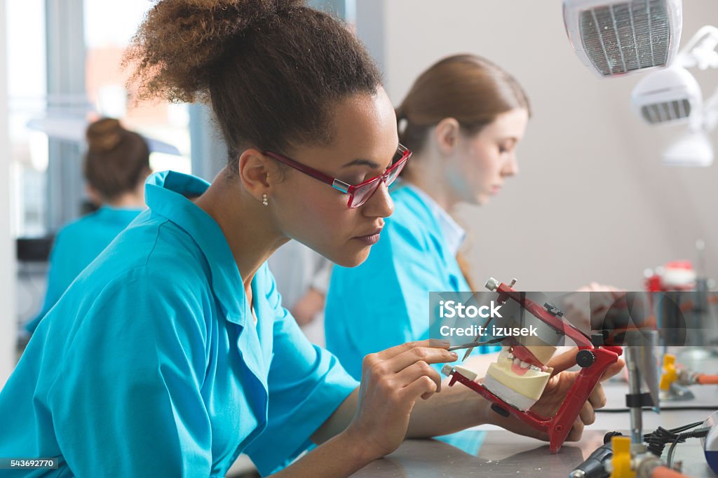 Female students learning prosthetic dentistry Young women wearing uniforms in a prosthodontic lab, learning prosthetic dentistry. Focus on afro american girl. Dental Health Stock Photo