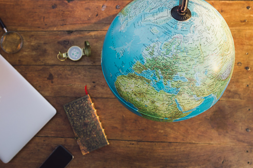 A map of the world with a notebook, a compass, a smart phone and a laptop over a wood table. Inspiration for travelers