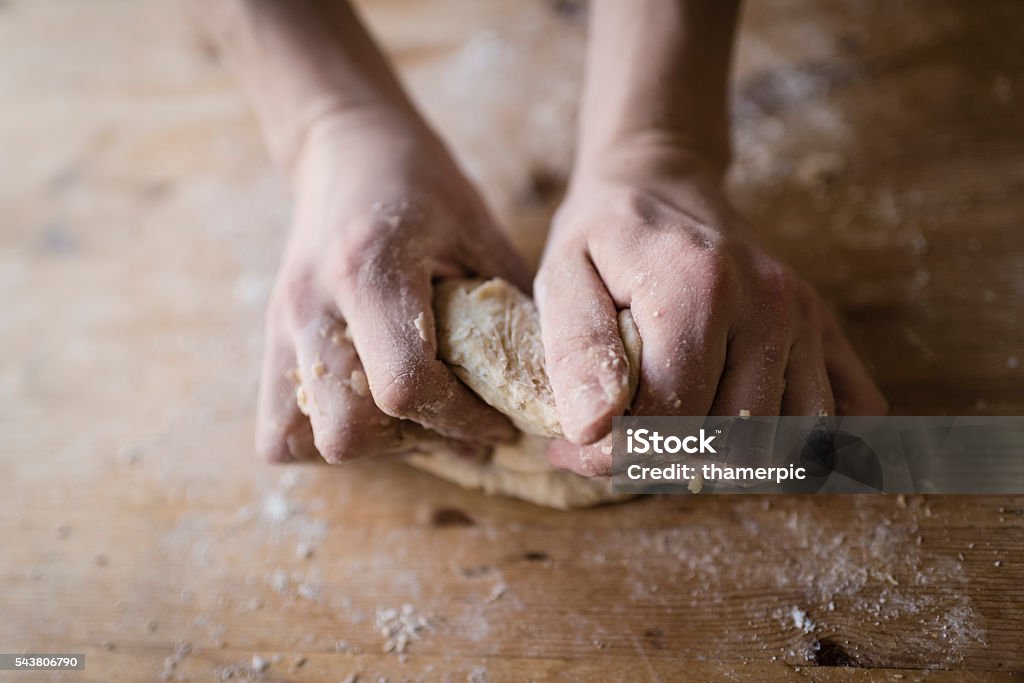 Two strong hands of a baker kneading homemade dough Close-up of two strong hands of a baker that are manually kneading dough on a rough, wooden kitchen table Craftsperson Stock Photo