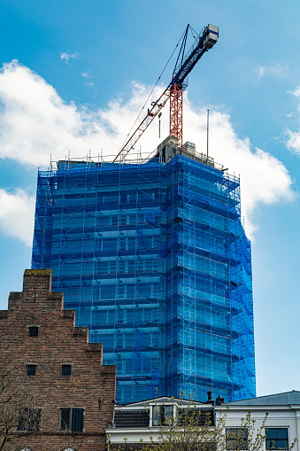 Modern  building site scaffolding  with blue covers and large crane behind stair shaped gable