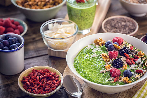 Green Breakfast Smoothie in Bowl with Superfoods on Top Green breakfast smoothie in bowl with superfoods like chia, quinoa, goji, fresh berries and sunflower seeds. antioxidant stock pictures, royalty-free photos & images