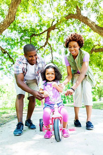 papa et maman apprend à sa fille à faire du tricycle - family cheerful family with one child texas photos et images de collection