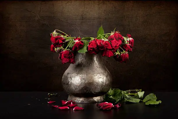 Photo of bouquet of dead red roses in silver vase, grunge background