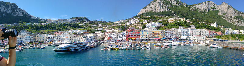 Capri, Italy  - May 31, 2016: Capri Island Landscape, Marina Grande harbour and mountains.Tourist taking photos of the landscape, idrofoil and boat in background, photo taken from Ferry boat in Capri harbor at early morning. 