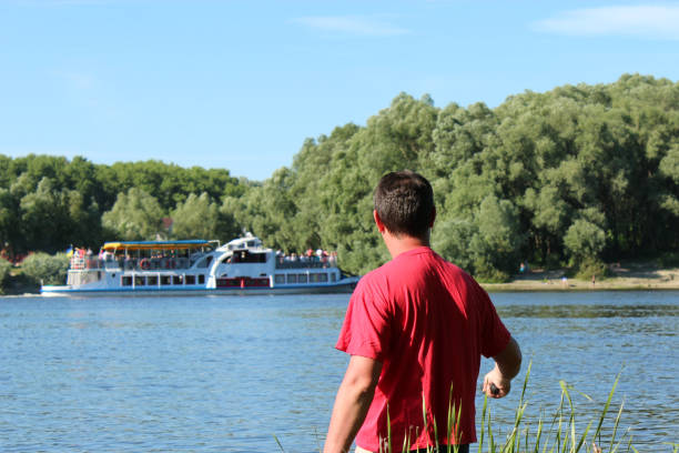 Wide shot of a 40-44-year-old Caucasian man kneeling praying calling out on a wooden jetty on a full lake of water overlooking mountains and woodlands with a moored rowboat with a dramatic purple orange coloured mood Cape Winelands South Africa