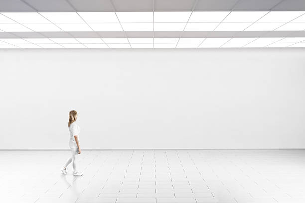 Woman walk in museum gallery with blank wall.