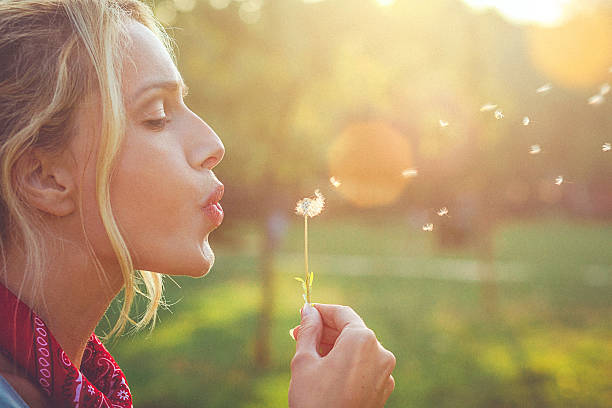 close-up de uma jovem feliz mulher loira soprando dente-de-leão - spring flower dandelion expressing positivity - fotografias e filmes do acervo
