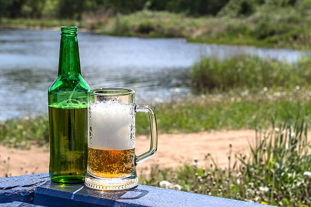 istock Bottle and mug frothy beer on table near lake 543978992