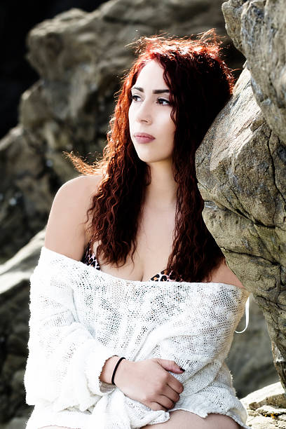 Hispanic Woman Outdoors On Rocks In Bikini With White Knitted Cover Looking To Side