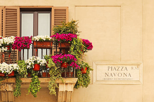 Rome, Italy - May 2, 2016: Piazza Navona street sign in Rome, Italy against an old building with a balcony with traditional Southern European window shutters. The balcony is decorated with white and pink flowers. 