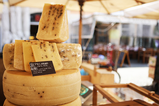 Italian Pecorino cheese for sale at Campo di Fiori market in Rome. Close-up is on the cheese, the rest of the market square is blur in the background.