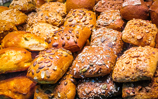 A stack of seeded multigrain rolls, fresh from the oven are displayed in a bakery shop window.