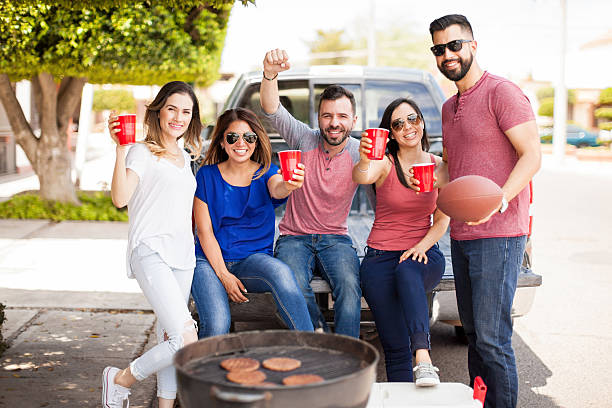 Group of people excited about a footbal game Young Hispanic friends celebrating the victory of their football team while drinking and having fun at a barbecue tailgate party photos stock pictures, royalty-free photos & images