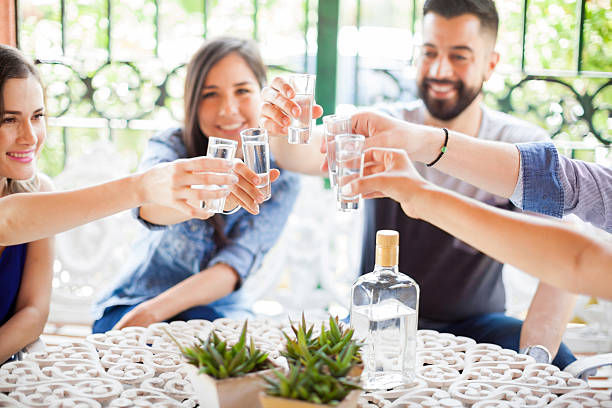 Group of friends making a toast with tequila Five friends raising their glasses and making a toast with tequila shots during a party outdoors tequila drink stock pictures, royalty-free photos & images