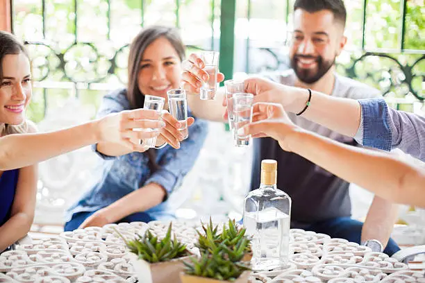 Five friends raising their glasses and making a toast with tequila shots during a party outdoors