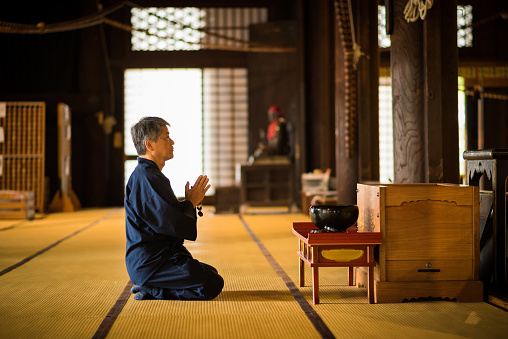 Senior Asian man praying inside of a Buddhist Temple