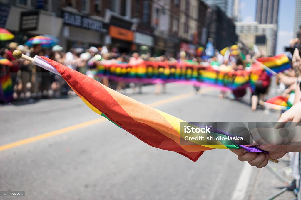 People participating in the World Pride Parade in Toronto. Spectators can be seen beside the path holding a rainbow flag. LGBTQ Adulation Stock Photo