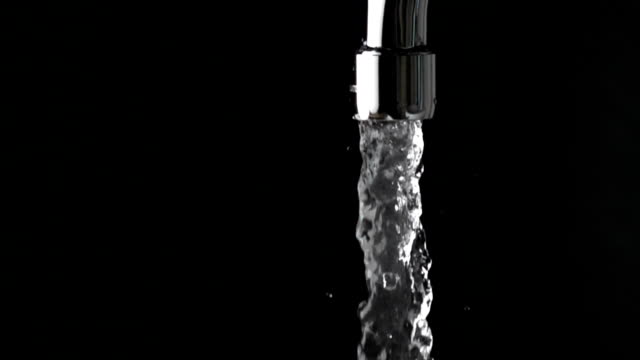 Close up slow motion shot of water running from tap against black background
