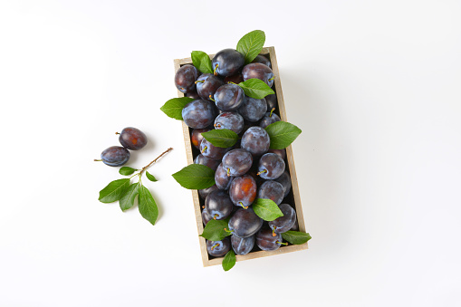 box of ripe plums on white background