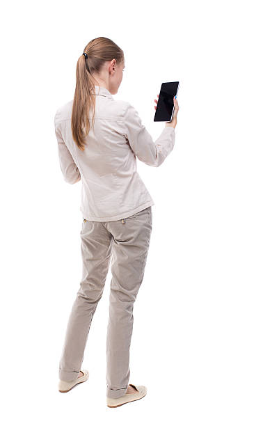 back view of standing young beautiful girl with tablet computer back view of standing young beautiful girl with tablet computer in the hands of. girl watching. Rear view people collection. backside view of person. Isolated over white background. A girl in a white jacket vertically holding the Tablet PC. pics of girls buttocks stock pictures, royalty-free photos & images