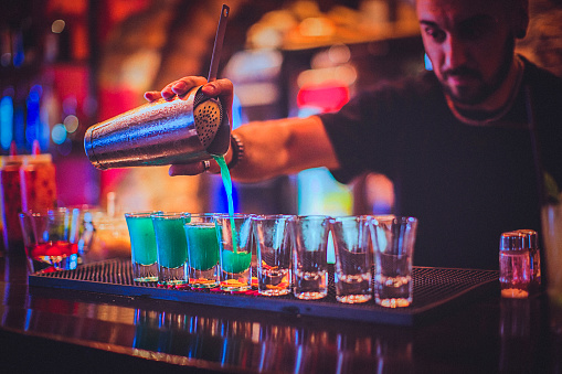 Close-up of a young bartender pouring cocktail in a nightlife cocktail bar. Selective focus. Focus on foreground.