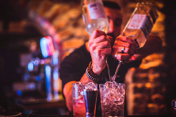Midsection of a young bartender preparing a cocktails in a nightlife cocktail bar. Selective focus. Focus on foreground.