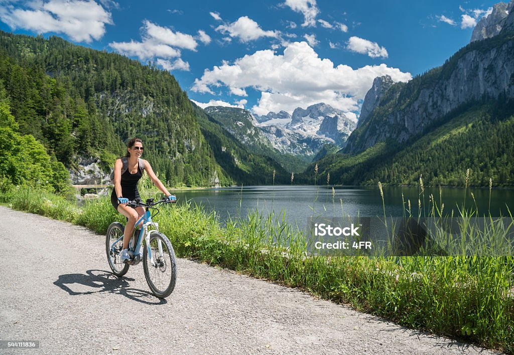 Woman on E-Bike Mountainbike in Nature, Lake Gosau, Dachstein Glacier Beautiful woman riding her E-Bike Mountainbike through the beautiful Austrian Alps by the lake Gosau (Gosausee) with the famous Dachstein Glacier in back. Nikon D810. Converted from RAW. Electric Bicycle Stock Photo