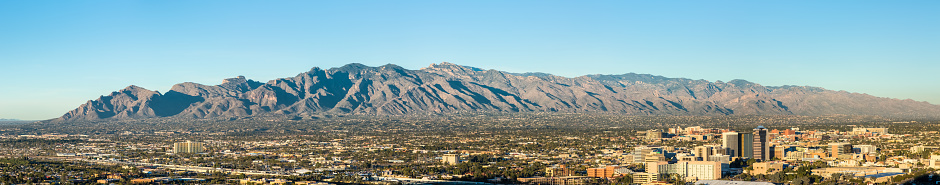 As seen from Sentinel Peak Park, downtown Tucson, Arizona, is located on the far side of the Santa Cruz River. The majestic Catalina Mountain Range can be seen in the distance under a clear blue sky.